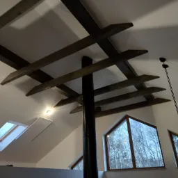 Wnętrze poddasza z drewnianymi belkami stropowymi, oknami dachowymi i kominem, wykończone płytami karton gips.