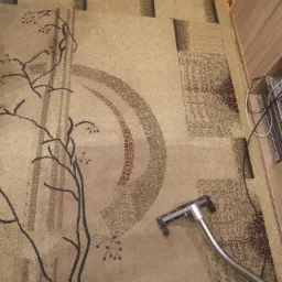 Czyszczenie beżowego dywanu ze wzorem drzewa w Kielcach przy użyciu profesjonalnego odkurzacza piorącego z niebieskim zbiornikiem.