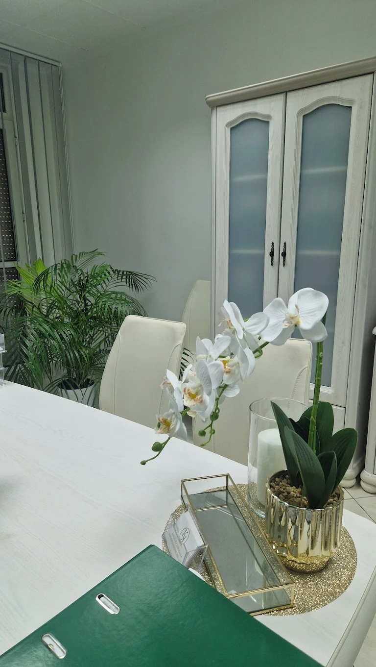 Jasne biuro z zielonym segregator, wizytówką, dekoracjami i kwiatami. W tle białe krzesła i szafa. Stonowana kolorystyka, minimalistyczny wystrój.