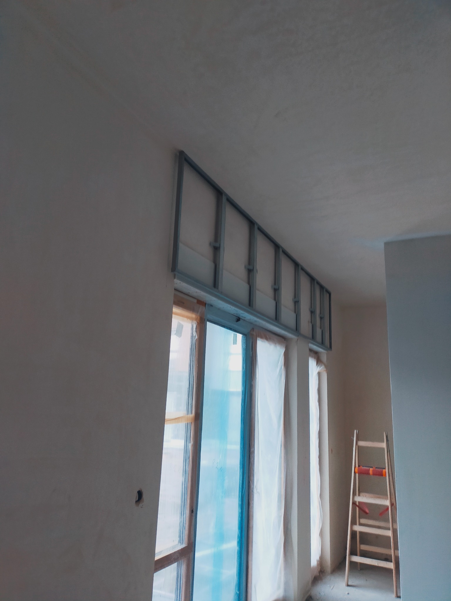 Metalowa konstrukcja pod zabudowę okna, widoczna drabina w tle, okno zabezpieczone folią.