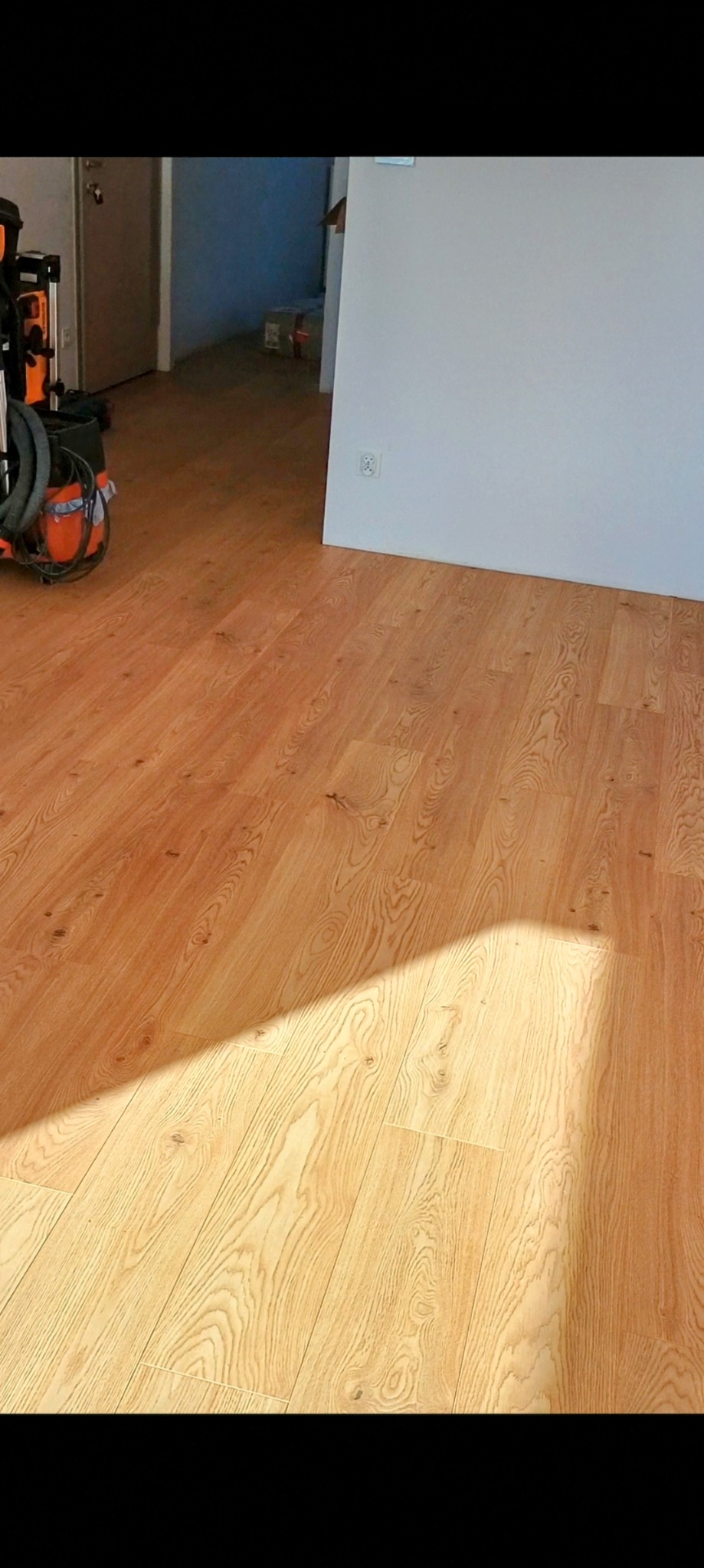 Jasny panel MDF ułożony w pokoju, widoczny odkurzacz i narzędzia w tle, cień na podłodze.