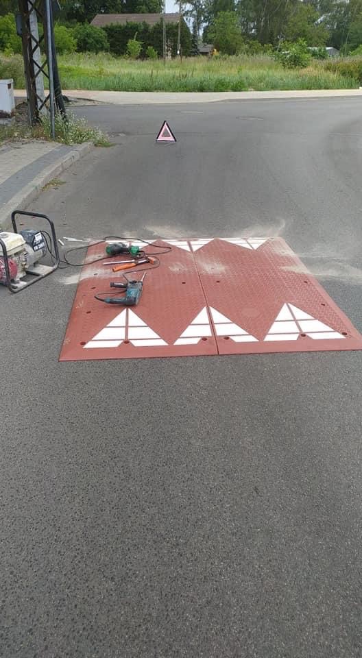 Instalacja progów zwalniających na jezdni, widoczny agregat prądotwórczy i narzędzia do montażu.