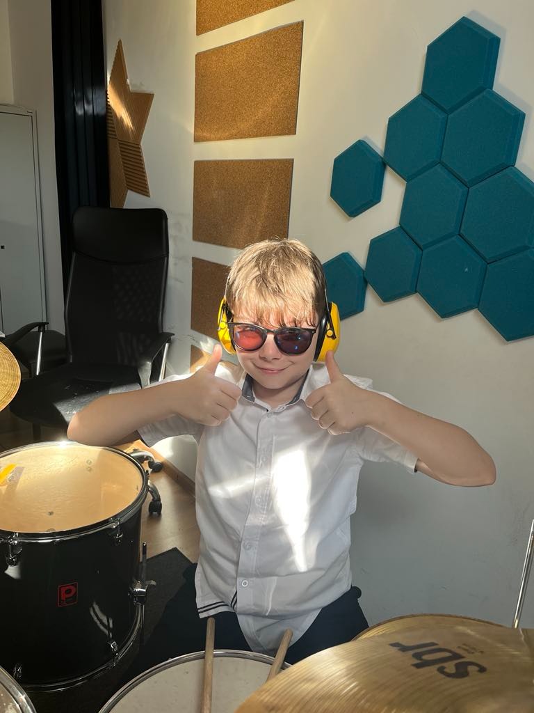 Chłopiec w słuchawkach i okularach 3D daje kciuki w górę za perkusją w studiu muzycznym z panelami akustycznymi w kształcie plastra miodu.