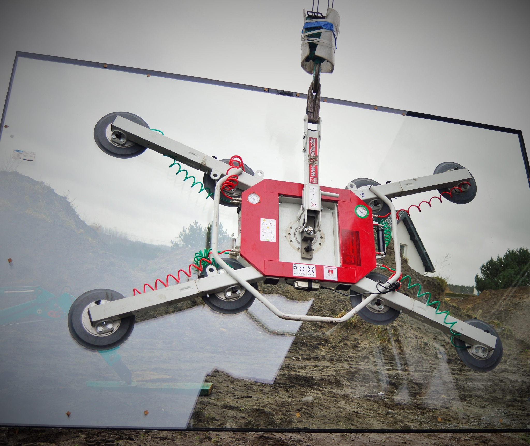 Duża szyba okienna podnoszona za pomocą przyssawkowej maszyny dźwigowej, widoczne odbicie krajobrazu w szkle.