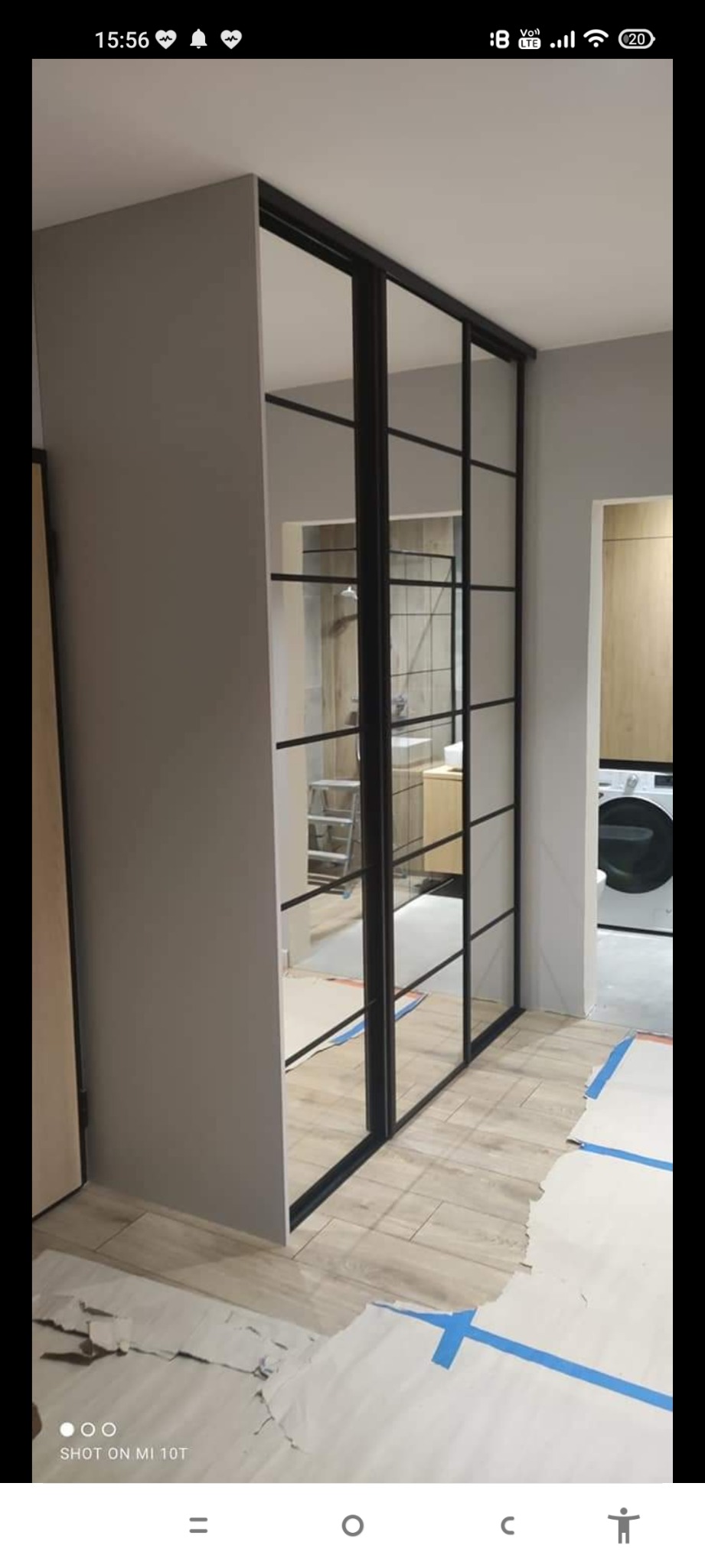 Montaż szafy wnękowej z czarnymi profilami i lustrzanymi drzwiami przesuwnymi, widoczne zabezpieczenia podłogi podczas prac.