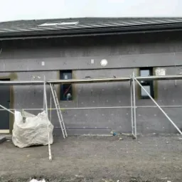 Dom jednorodzinny w trakcie montażu płyt izolacyjnych na elewacji, widoczne rusztowanie, drabina i worki z materiałami budowlanymi.