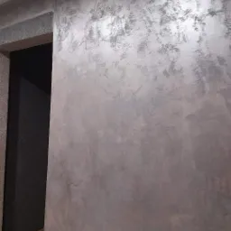 Ściana wewnętrzna z dekoracyjną fakturą w odcieniach szarości i srebra, widoczny fragment futryny drzwiowej i podłogi.