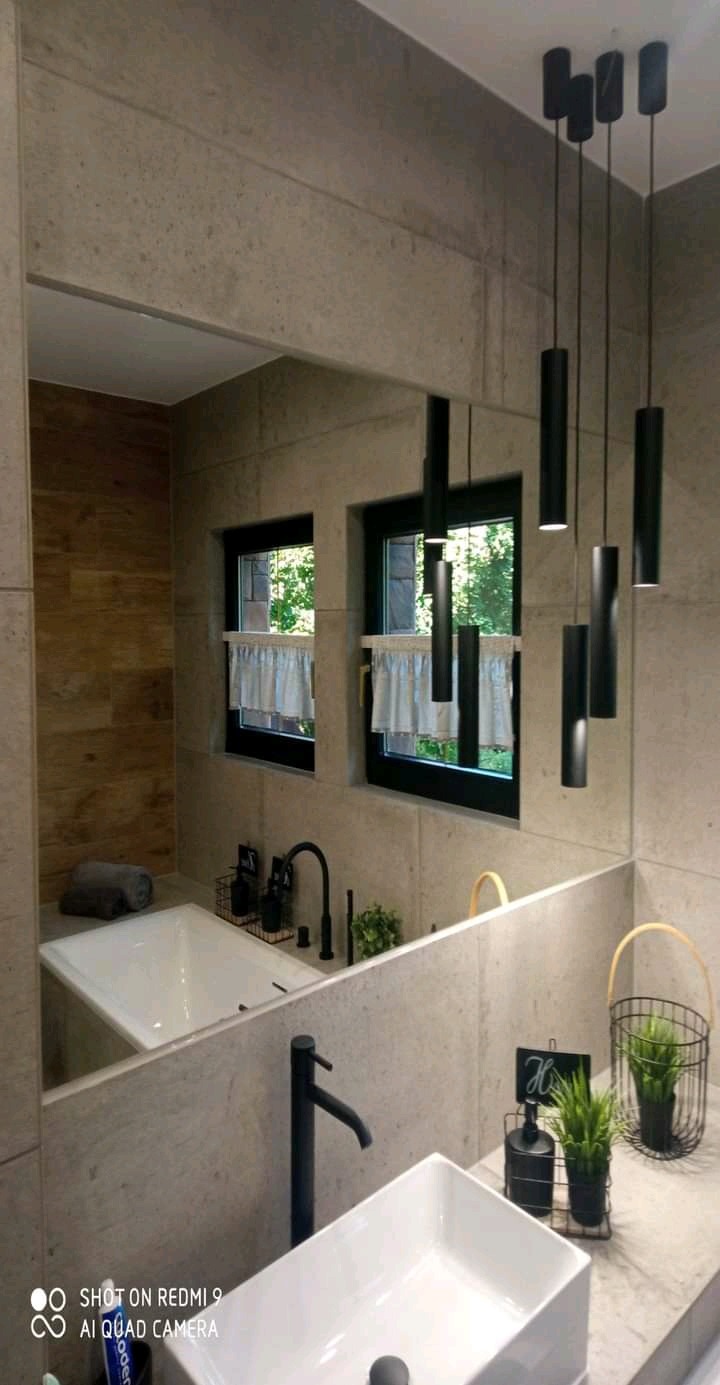 Nowoczesna łazienka z wanną, umywalką nablatową i czarną armaturą, oświetlona wiszącymi lampami tubami, z widokiem na zieleń za oknem.