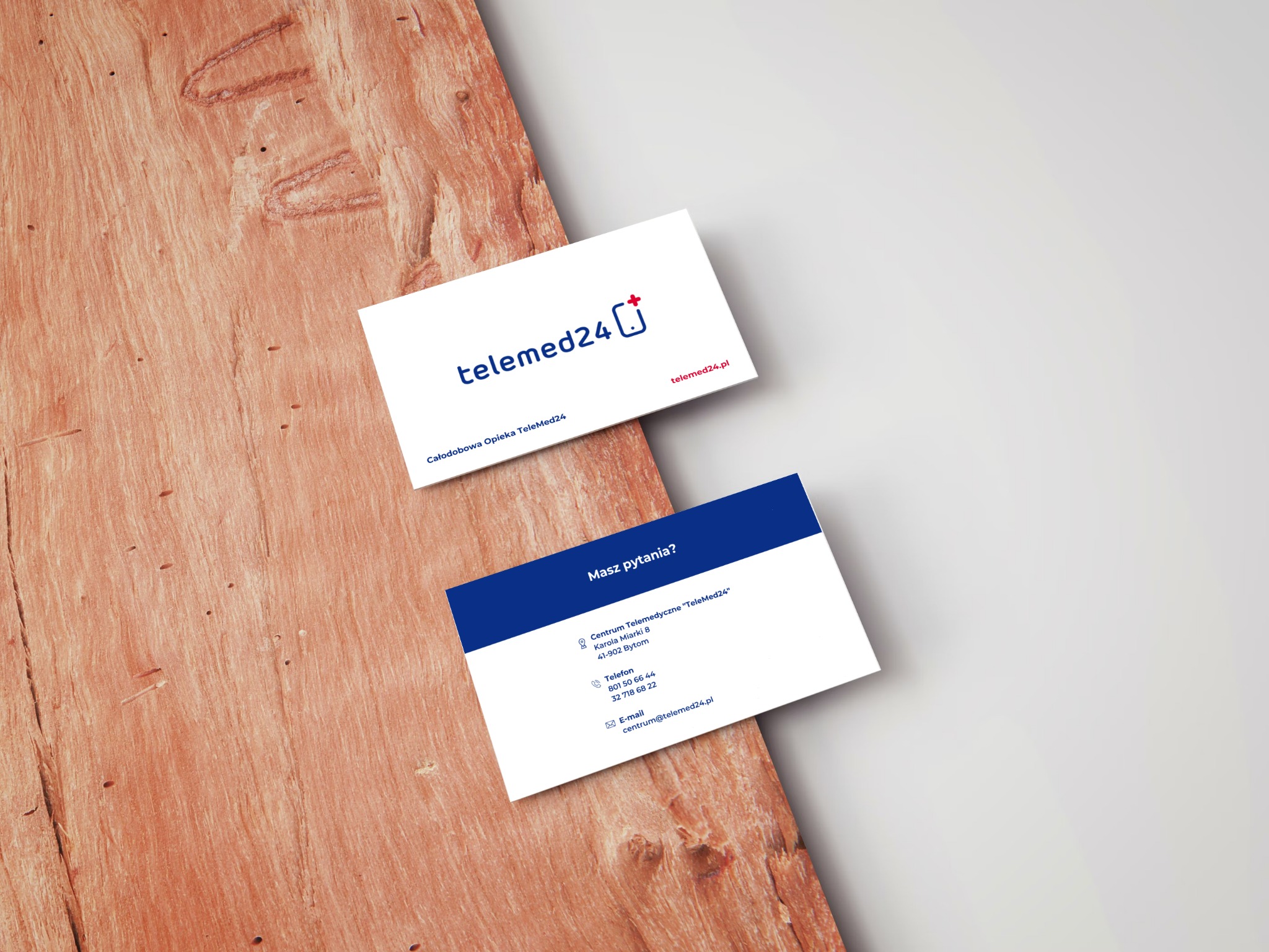 Dwie wizytówki firmy telemed24.pl leżące na drewnianej powierzchni z widoczną fakturą. Górna wizytówka prezentuje logo i hasło firmy, dolna zawiera dane kontaktowe.