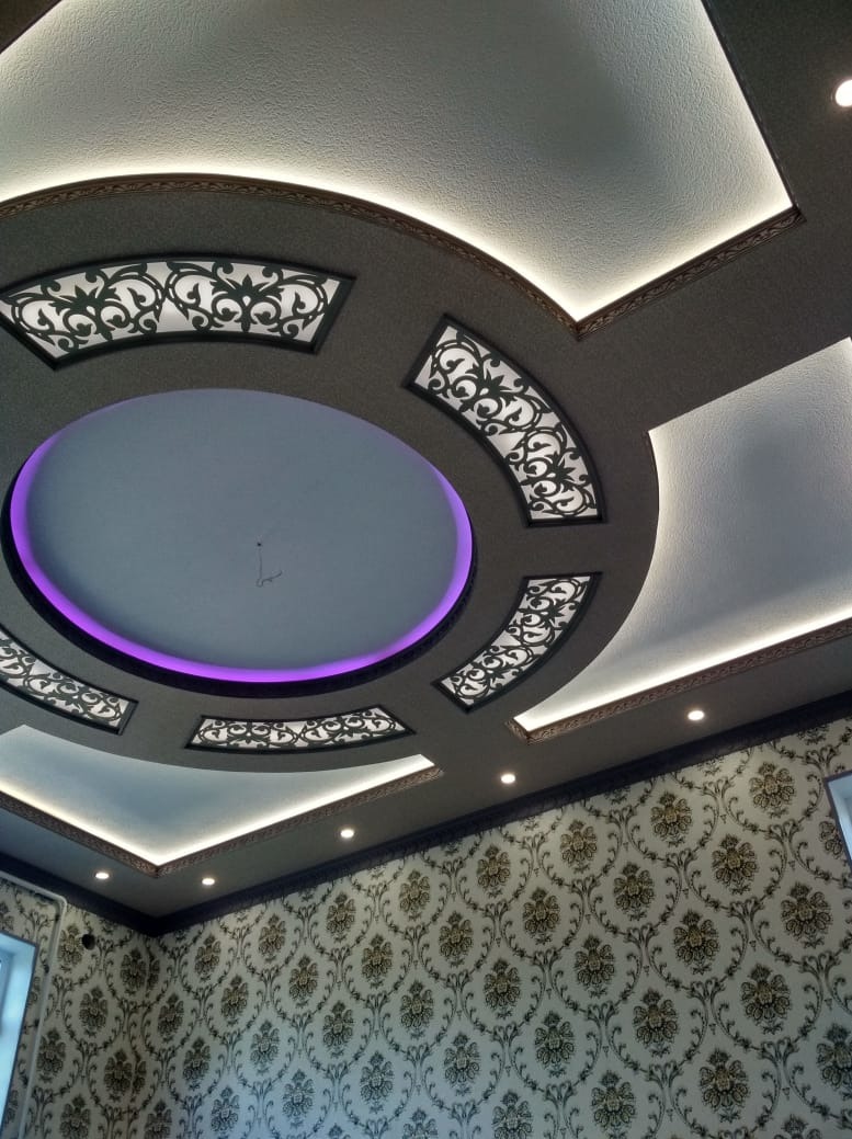 Dekoracyjny sufit podwieszany z oświetleniem LED i wzorzystą tapetą w tle. Okrągły element z fioletową obwódką i ażurowe panele dodają elegancji wnętrzu.