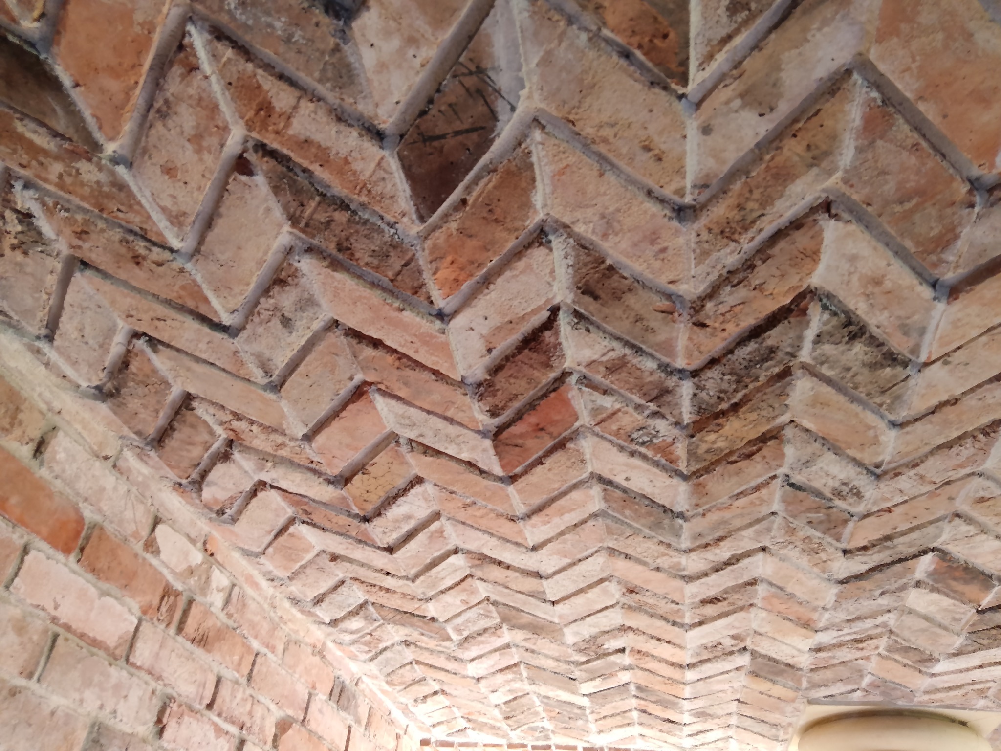 Ceglany sufit ułożony we wzór jodełki, z widocznymi spoinami i naturalną kolorystyką cegieł, oświetlony z dołu.