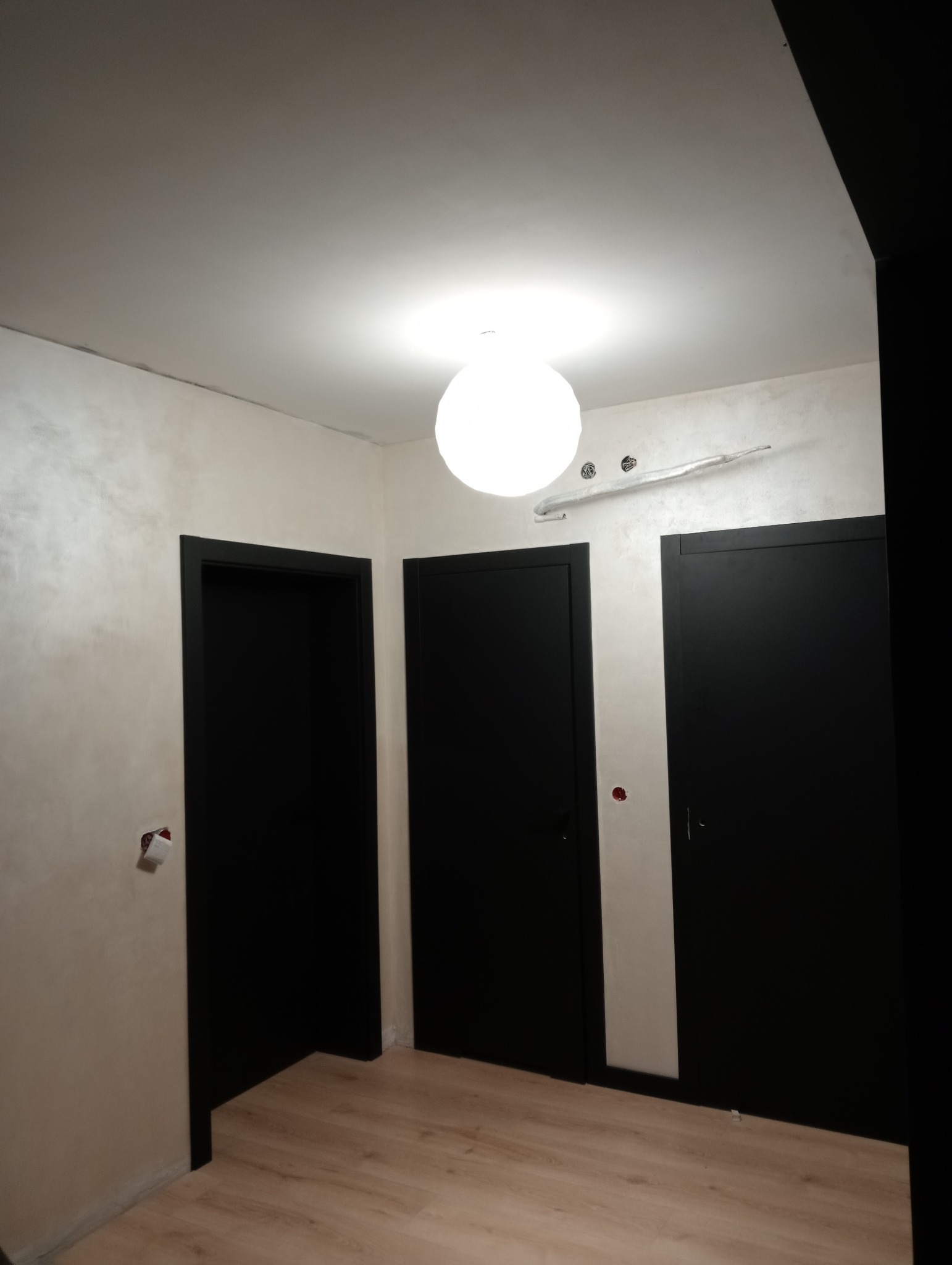 Korytarz po odświeżeniu z trzema czarnymi drzwiami, kremowymi ścianami z efektem dekoracyjnym i okrągłą lampą sufitową.