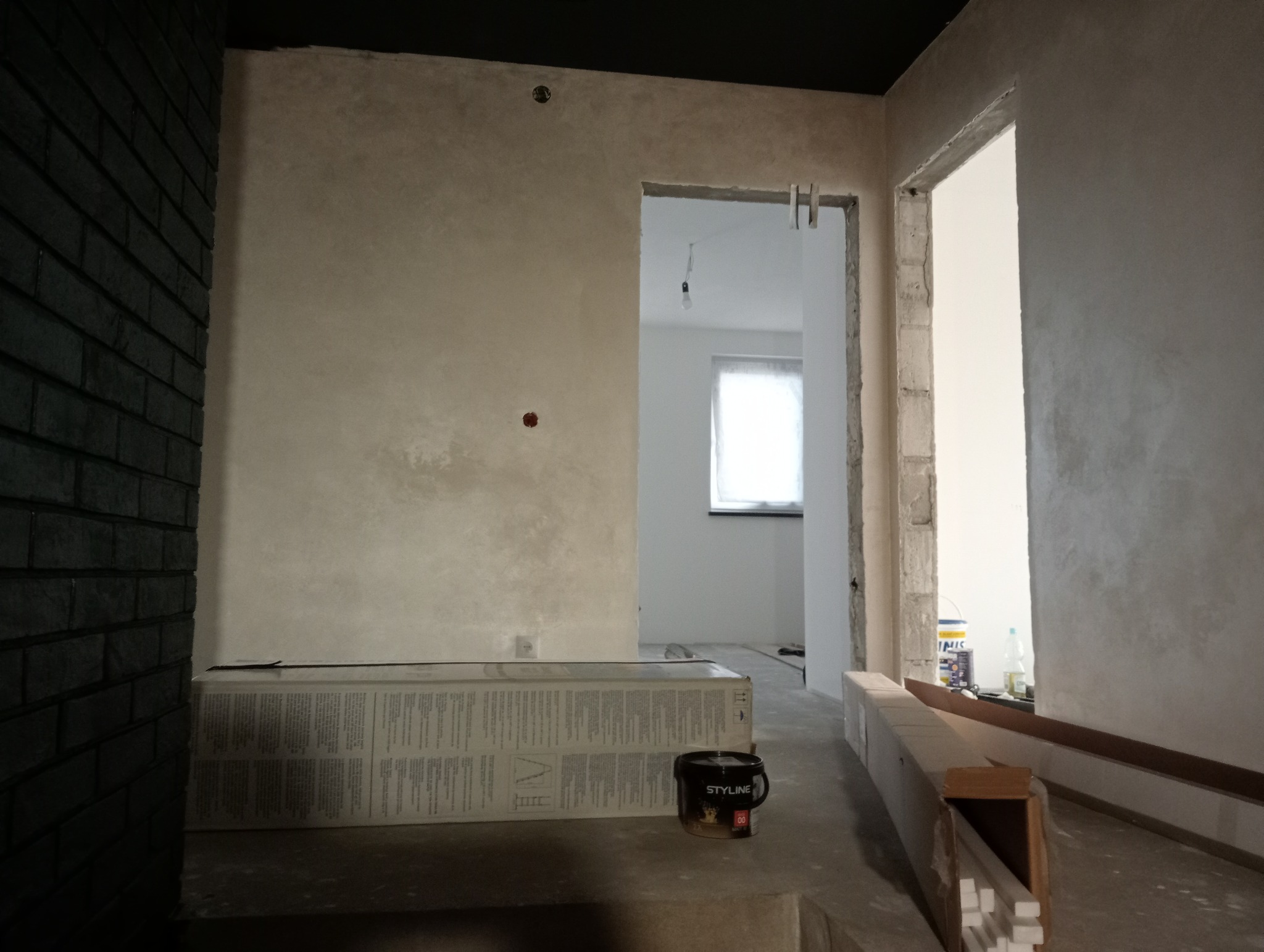 Ściana z nałożoną dekoracyjną gładzią w odcieniach beżu i szarości, widoczne puszki farb i materiały wykończeniowe, wnętrze w trakcie remontu z surowymi framugami drzwi.