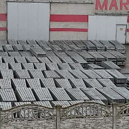 Stosy prefabrykowanych paneli ogrodzeniowych z betonu architektonicznego składowane obok budynku magazynowego z czerwonymi pasami.