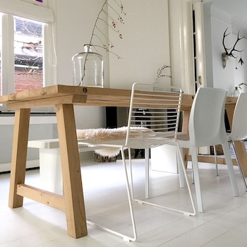 Jasne wnętrze jadalni w Łomiankach: drewniany stół na kozłach, białe krzesła o ażurowej konstrukcji, biała podłoga, za stołem kominek i dekoracje ścienne, w tym poroże jelenia.