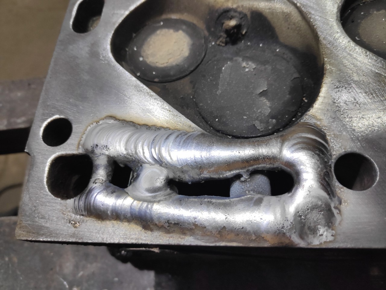 Szczegółowe ujęcie spawu na aluminiowej głowicy silnika samochodowego, widoczne ślady obróbki i nierówności powierzchni.