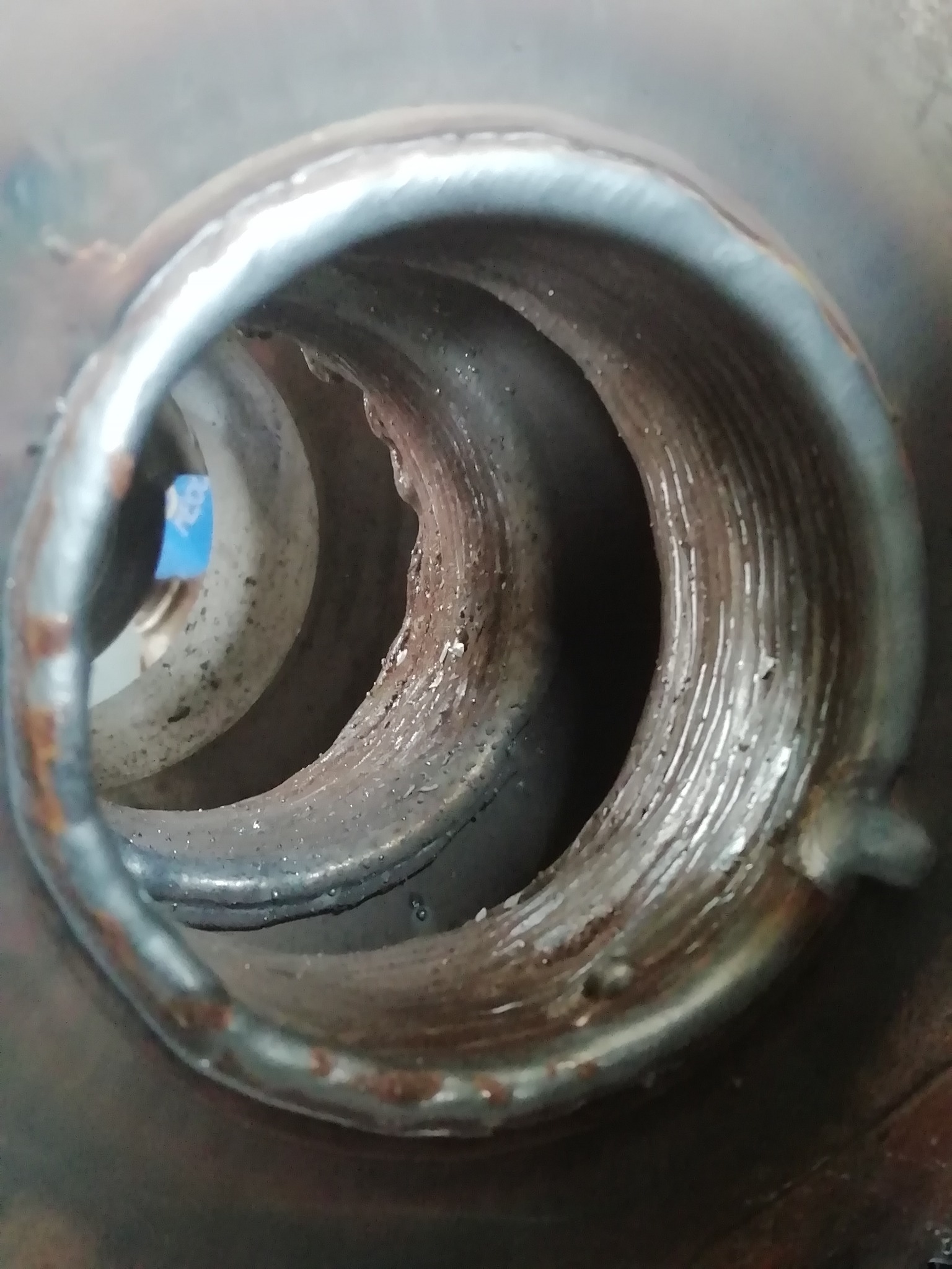 Wewnętrzny widok spiralnej rury, prawdopodobnie elementu wymiennika ciepła, z widocznymi śladami spawania i korozji.