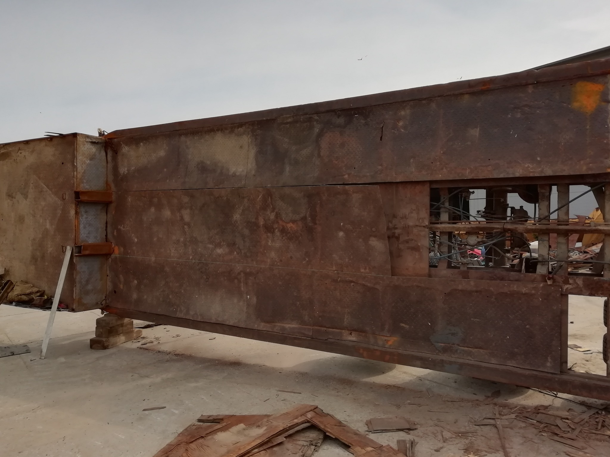 Konstrukcja metalowa z widocznymi śladami rdzy, oparta na betonowych blokach, z elementami kratownicy w tle, sugerująca etap budowy lub demontażu.