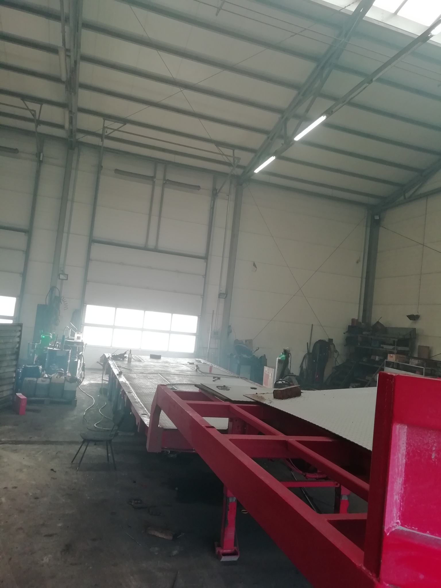 Wnętrze hali produkcyjnej z widoczną platformą transportową w trakcie budowy, elementy konstrukcyjne w kolorze czerwonym, widoczne narzędzia i sprzęt spawalniczy w tle.