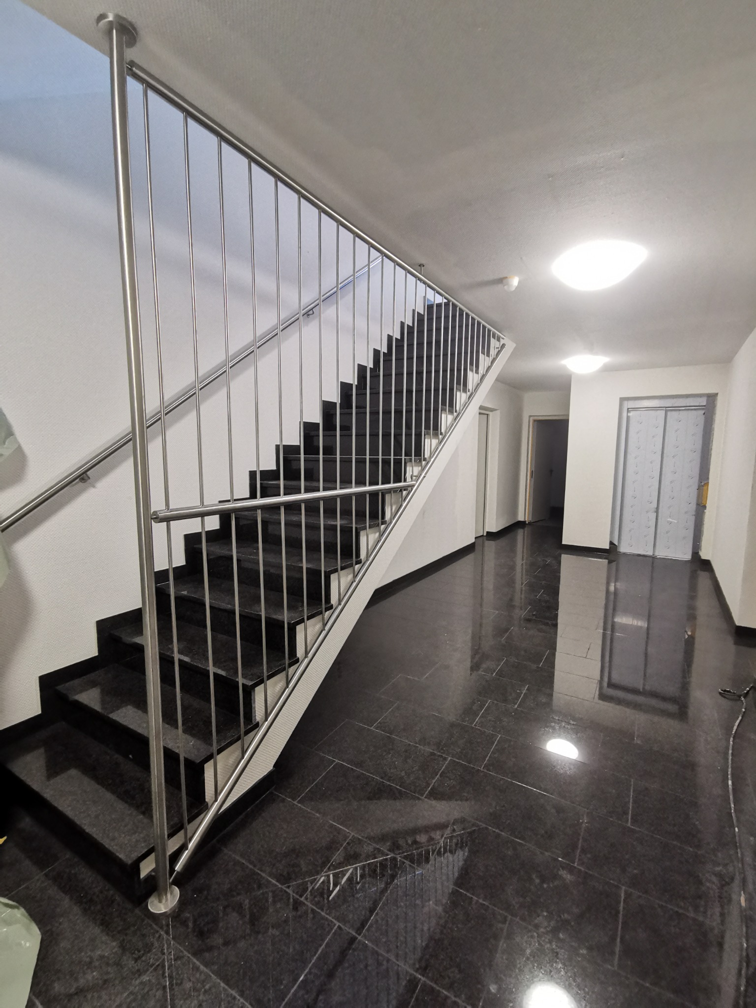 Schody z czarnego granitu z metalową balustradą z pionowymi prętami, widok z dołu klatki schodowej w budynku.