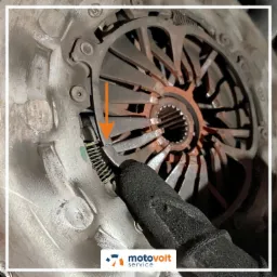 Zbliżenie na tarczę sprzęgła samochodowego z widocznym mechanizmem dociskowym, z wyraźnym wskazaniem na sprężynę, sprawdzaną przez pracownika w rękawicy roboczej.