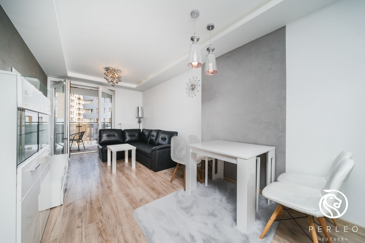 Nowoczesny salon z czarną skórzaną sofą narożną, białym stolikiem kawowym, białym stołem jadalnym i krzesłami, z wyjściem na balkon w tle.