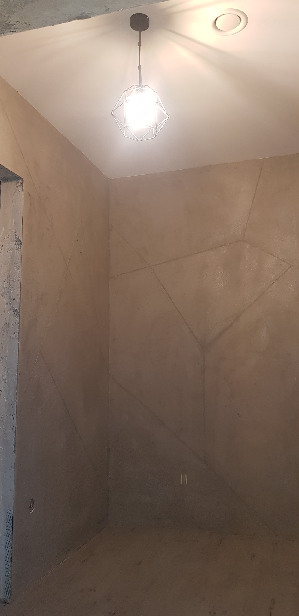 Ściana w pokoju po nałożeniu dekoracyjnej szpachli z geometrycznym wzorem, oświetlona przez nowoczesną lampę wiszącą z metalową konstrukcją.