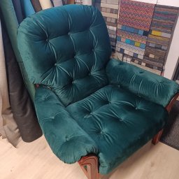 Tapicer - Szmaragdowy fotel tapicerowany z guzikami, obok rolki materiałów i próbniki tkanin