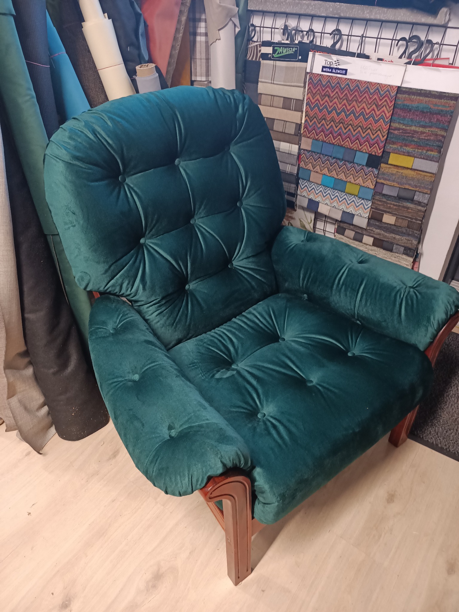 Szmaragdowy fotel tapicerowany z guzikami, obok rolki materiałów i próbniki tkanin