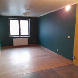 Paulina Michniak Wykończenia Wnętrz - Pokój po zmianie koloru ścian na butelkową zieleń i żółty, z nową drewnianą podłogą, widoczne gniazdka elektryczne.