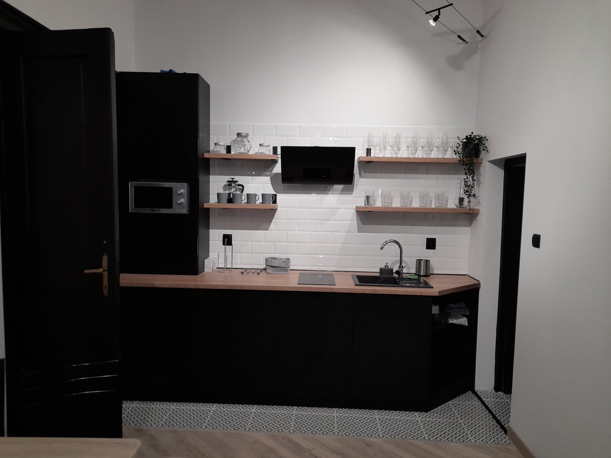 Nowoczesna kuchnia w czerni i bieli z drewnianymi akcentami, oświetleniem punktowym i wzorzystą podłogą.