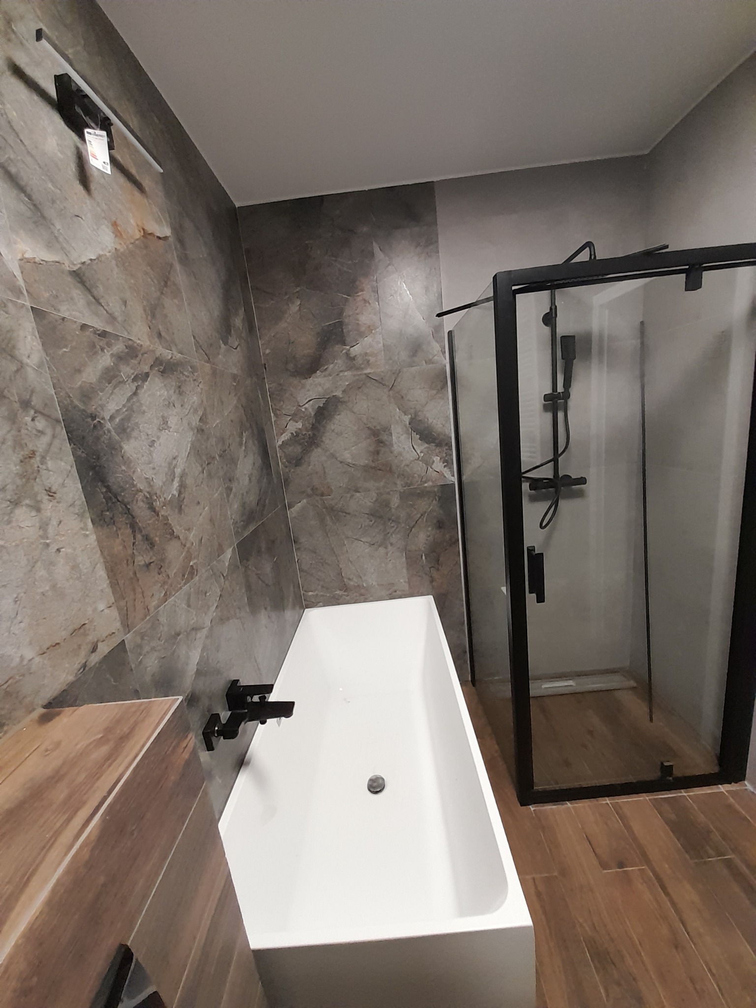 Nowoczesna łazienka z kabiną prysznicową z czarną ramą, białą wanną i marmurowymi płytkami na ścianie.