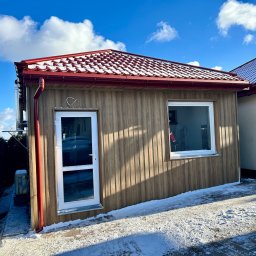 Kosar-bud - Nowoczesny, drewniany budynek z czerwoną dachówką ceramiczną pokrytą śniegiem, widoczny w zimowej scenerii. Elewacja pionowa, okno PCV, rynna w kolorze dachu.