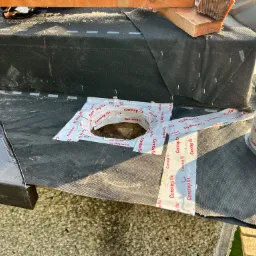 Fragment dachu w trakcie montażu z użyciem taśmy uszczelniającej Corotop fix, widoczne narzędzia i elementy konstrukcyjne. Czarna membrana dachowa zabezpieczona przed wilgocią.