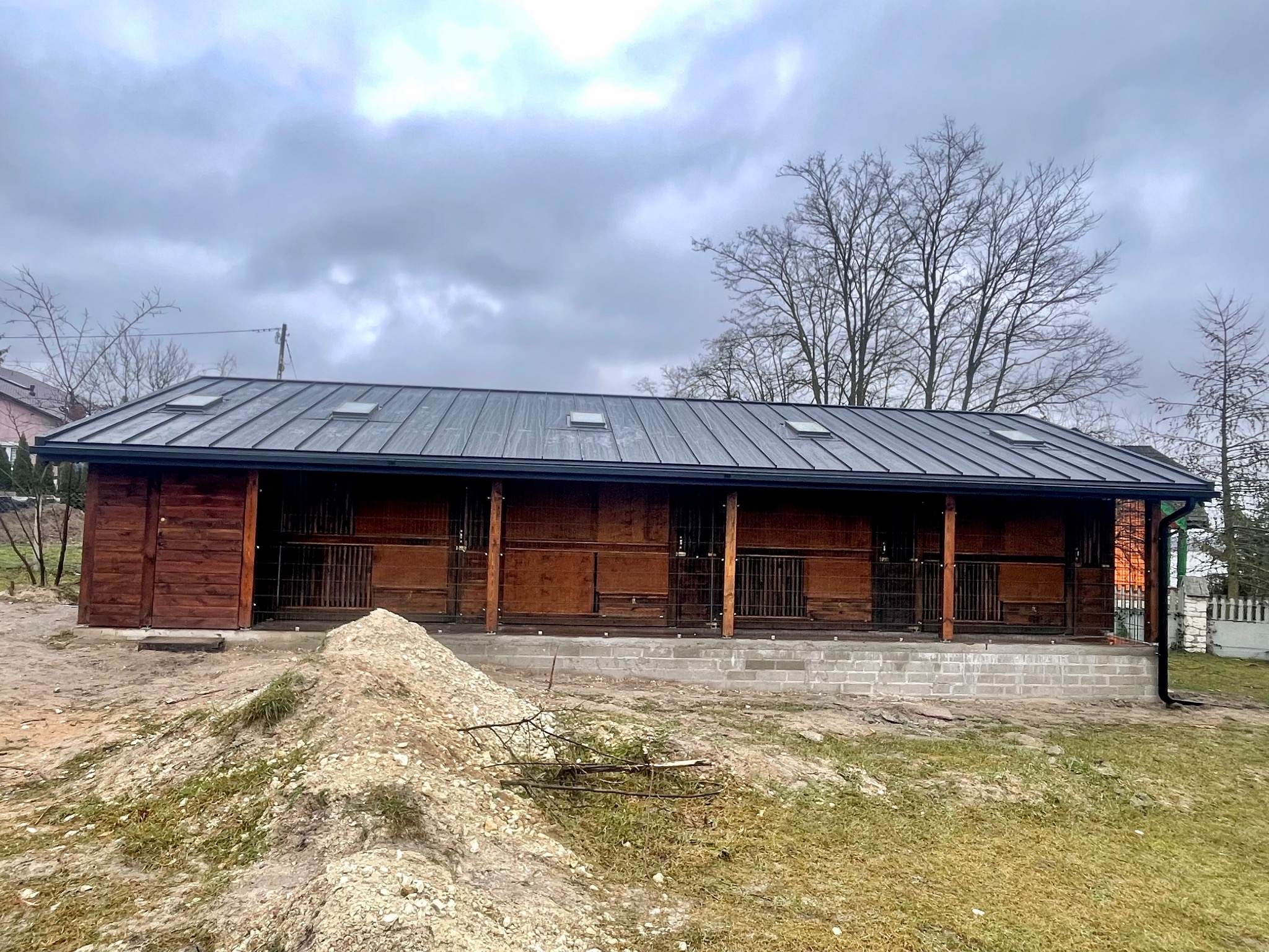 Nowo wybudowany budynek z ciemnego drewna z ciemnoszarą metalową konstrukcją dachową i świetlikami, w trakcie prac wykończeniowych.