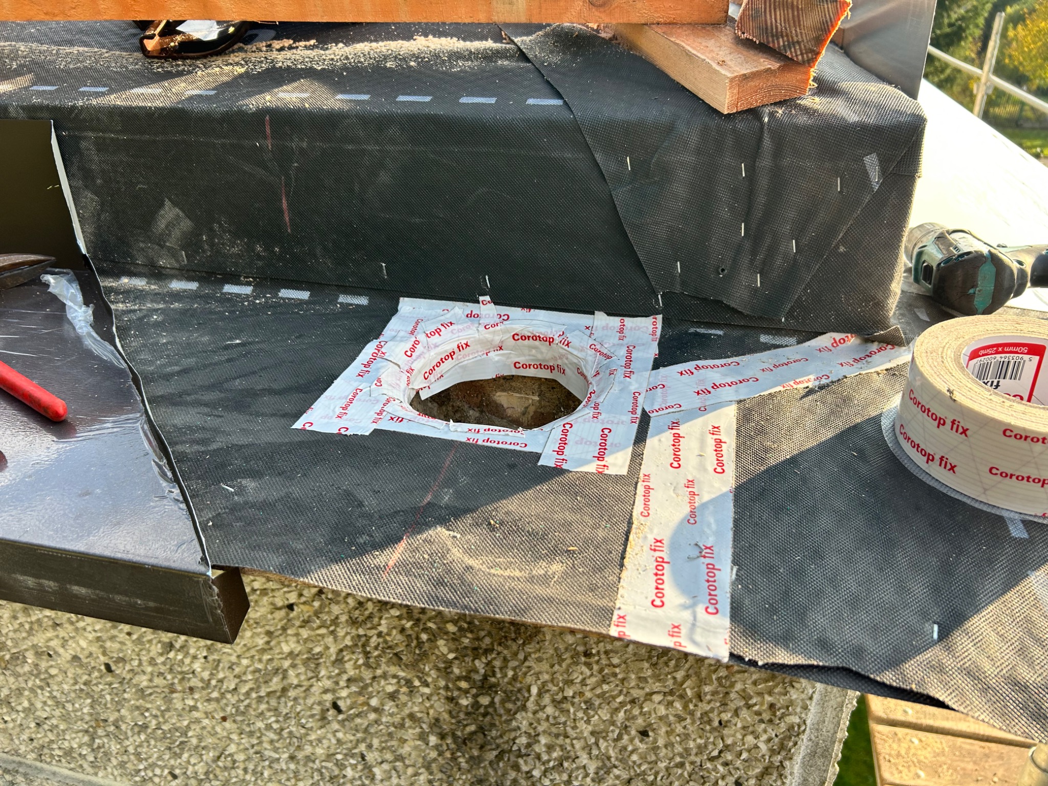 Fragment dachu w trakcie montażu z użyciem taśmy uszczelniającej Corotop fix, widoczne narzędzia i elementy konstrukcyjne. Czarna membrana dachowa zabezpieczona przed wilgocią.