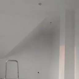 Świeżo otynkowane poddasze ze skosami, widoczne punkty instalacji elektrycznej i fragment drabiny malarskiej.