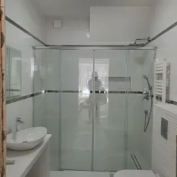 Nowoczesna łazienka z przeszkloną kabiną prysznicową typu walk-in, umywalką nablatową na białej szafce, wiszącą toaletą i grzejnikiem drabinkowym, całość utrzymana w jasnej kolorystyce.