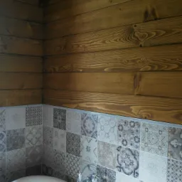 Drewniana boazeria na ścianie nad wanną z baterią i dekoracyjnymi płytkami w łazience.