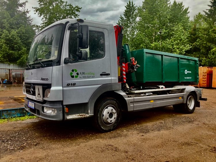 Srebrna ciężarówka Mercedes Atego 918 z zielonym kontenerem na gruz, z widocznym logo firmy AJRecykling i numerem telefonu, stojąca na ziemi w pochmurny dzień.