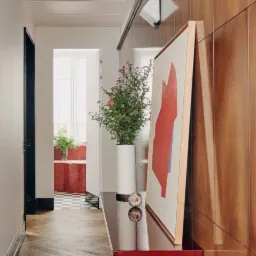 Korytarz z parkietem ułożonym w jodełkę, drewnianą boazerią na ścianie i konsolą z kwiatami oraz abstrakcyjnym obrazem, widok w głąb mieszkania.