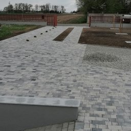 DAMTES USŁUGI WIELOBRANŻOWE DAMIAN DROBNY - Ułożona kostka brukowa w odcieniach szarości tworząca ścieżkę i podjazd. W tle widoczne ogrodzenie i drzewa. Minimalistyczny styl, świeżo po realizacji.