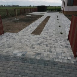 DAMTES USŁUGI WIELOBRANŻOWE DAMIAN DROBNY - Ułożona kostka brukowa w odcieniach szarości tworząca ścieżkę i podjazd do domu. Elementy dekoracyjne z kamienia i ziemi. Widok z góry na posesję.