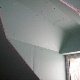 Firma Remontowo Budowlana Fachbud Piotr Grzegorzek - Montaż płyt gipsowo-kartonowych na poddaszu, widoczne wkręty mocujące i okno z folią ochronną.