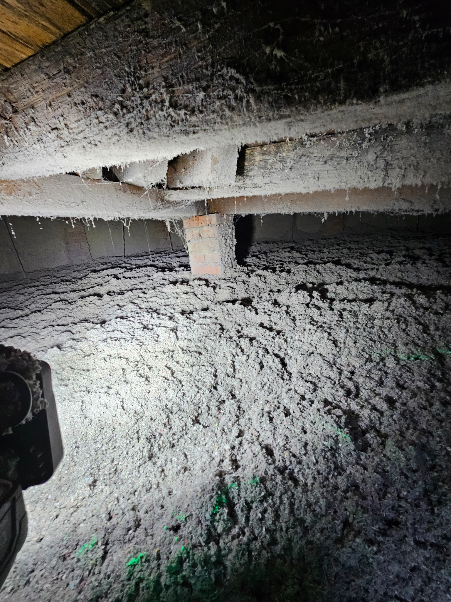 Poddasze po ociepleniu: widoczne drewniane belki pokryte białą pianką izolacyjną, na podłodze gruba warstwa szarej wełny mineralnej. Oświetlenie punktowe.