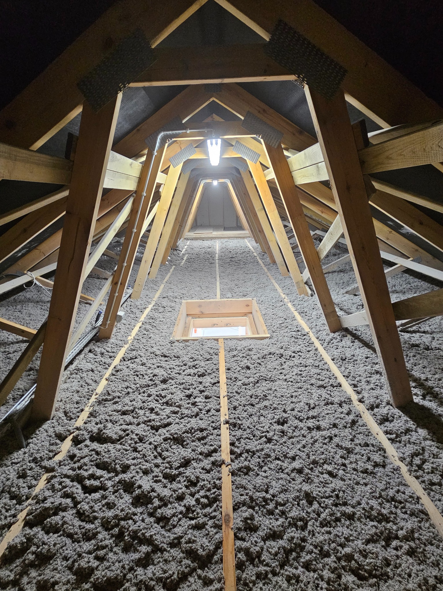 Poddasze z drewnianą konstrukcją i warstwą izolacyjną z wełny mineralnej, widok z dołu, oświetlone lampą. Element okna połaciowego.