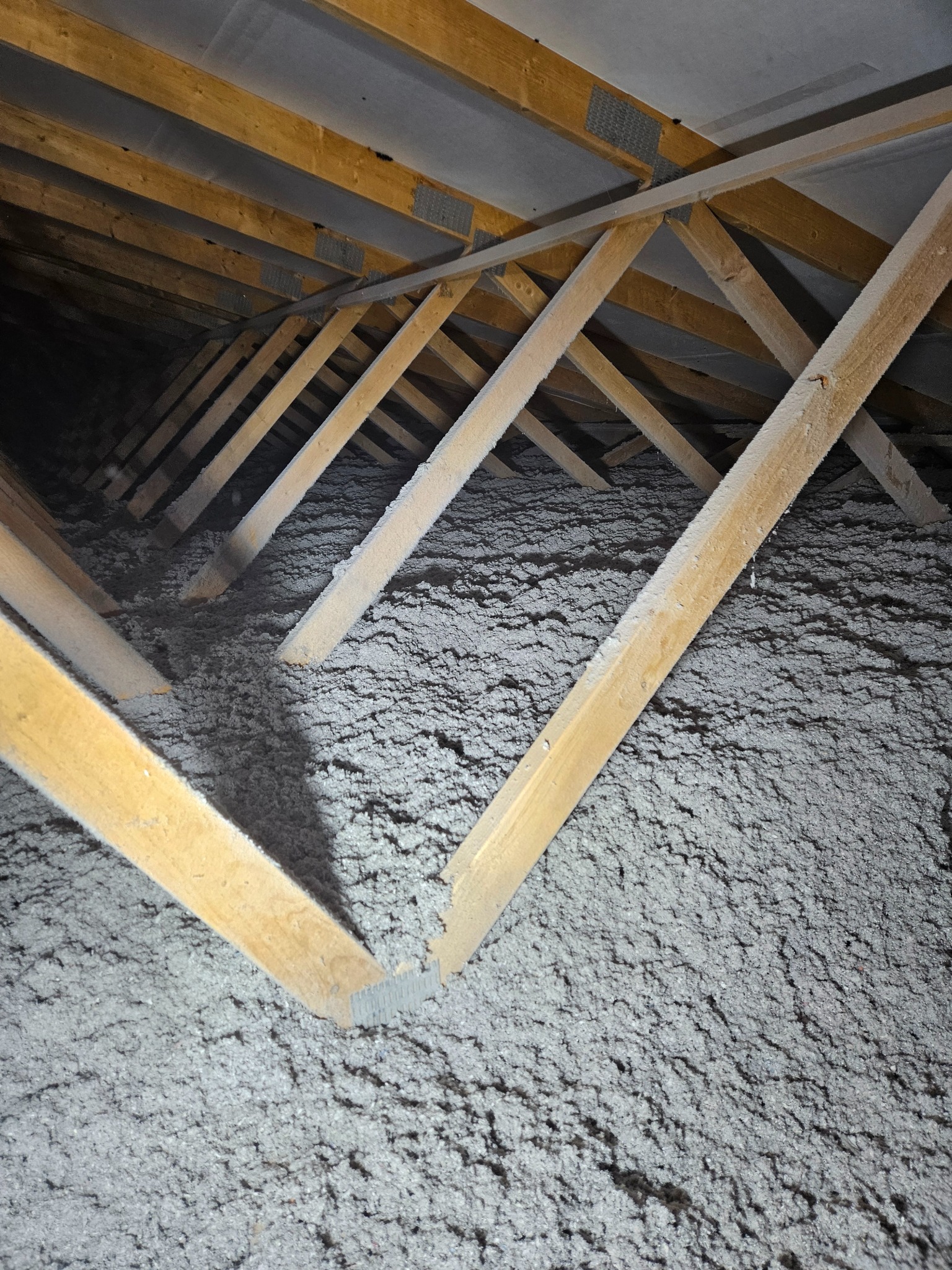 Poddasze z widoczną izolacją z wełny mineralnej między drewnianymi krokwiami. Elementy konstrukcji dachu w surowym drewnie. Nierówna powierzchnia izolacji.