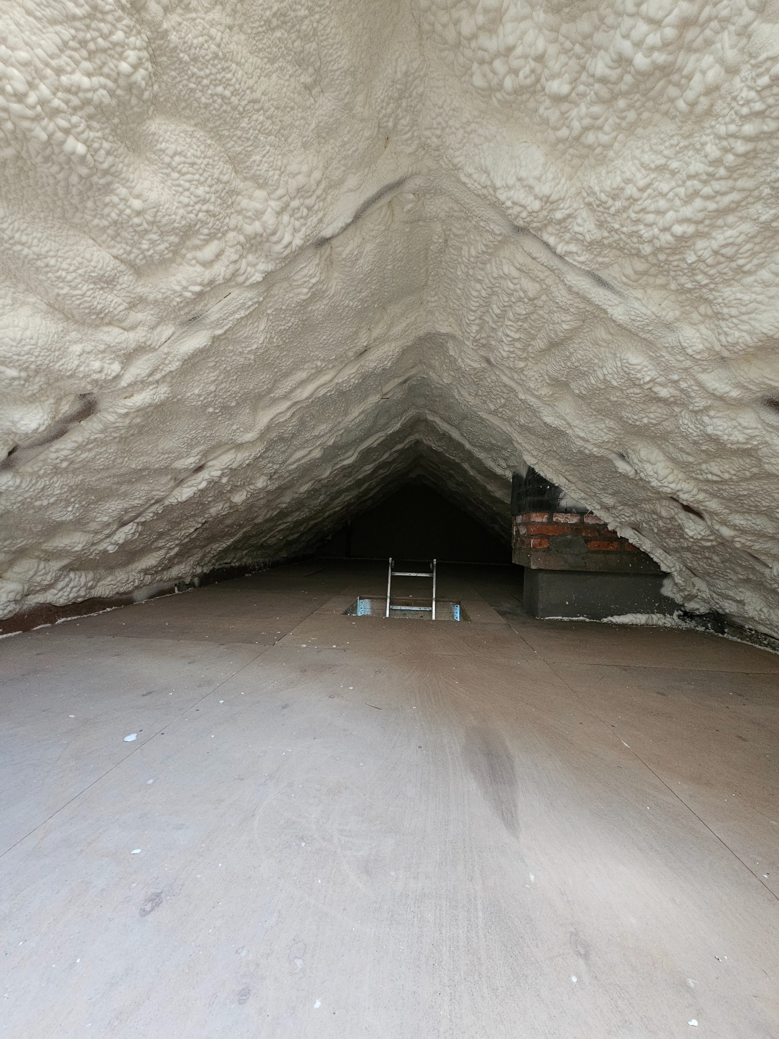 Poddasze po ociepleniu pianką PUR, widoczna warstwa izolacji pokrywająca skośne ściany i sufit. W tle drabina i fragment komina.