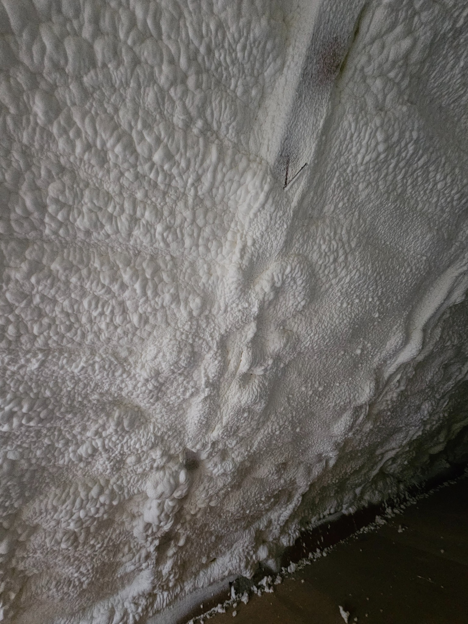 Poddasze po aplikacji białej pianki izolacyjnej, widoczna struktura piany i pojedynczy metalowy element mocujący. Kąt ujęcia od dołu, fragment podłogi.