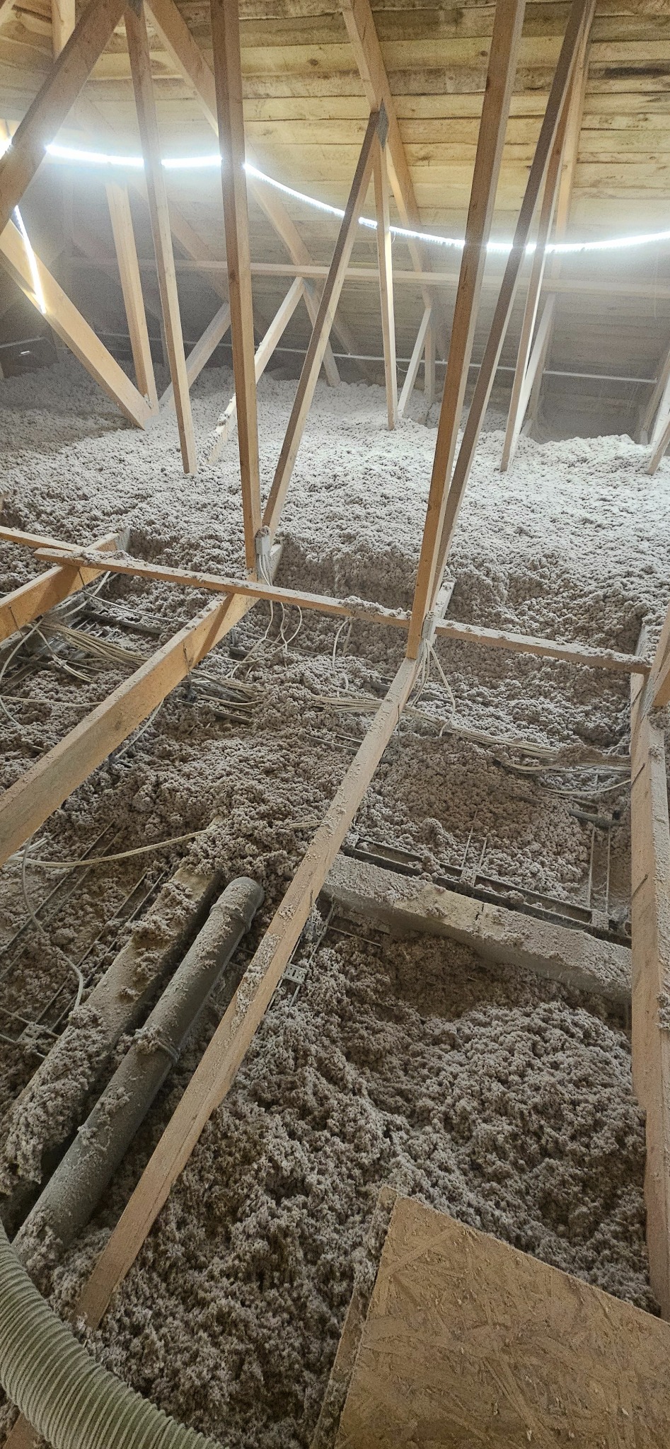 Poddasze z widoczną konstrukcją drewnianą i warstwą izolacji z wełny mineralnej, przewody elektryczne, rury wentylacyjne. Ocieplenie wykonane w szarym odcieniu.